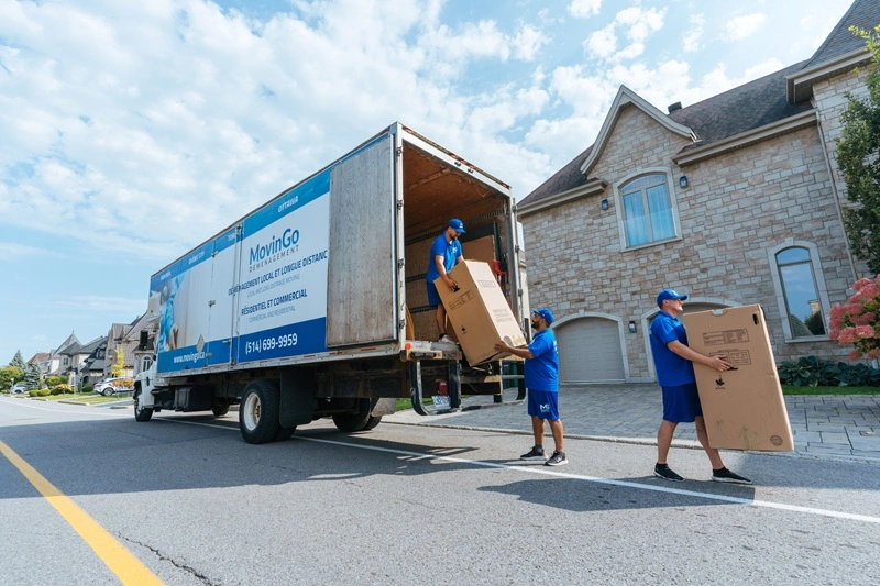 Trois déménageurs MovinGo déchargent des boîtes du camion devant une maison